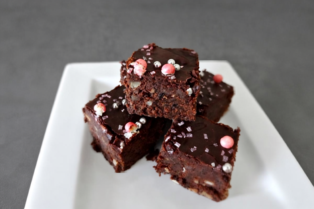 Brownie aux haricots noirs sans gluten, carrés empilés sur une assiette blanche avec glaçage chocolat et perles sucrées roses