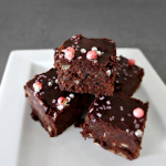 Brownie aux haricots noirs sans gluten, carrés empilés sur une assiette blanche avec glaçage chocolat et perles sucrées roses