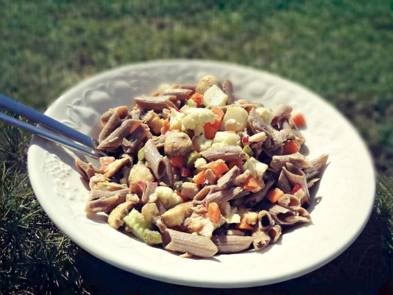 Salade de pâtes de sarrasin au thon dans un saladier blanc posé sur l'herbe dans le jardin