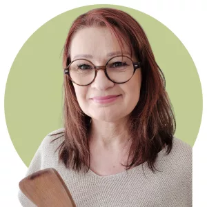 Photo de Véro du blog Bienvenuechezvero.fr
Cheveux brun-roux mi-longs avec des lunettes rondes brunes et qui sourie. Avec une spatule en bois dans la main
