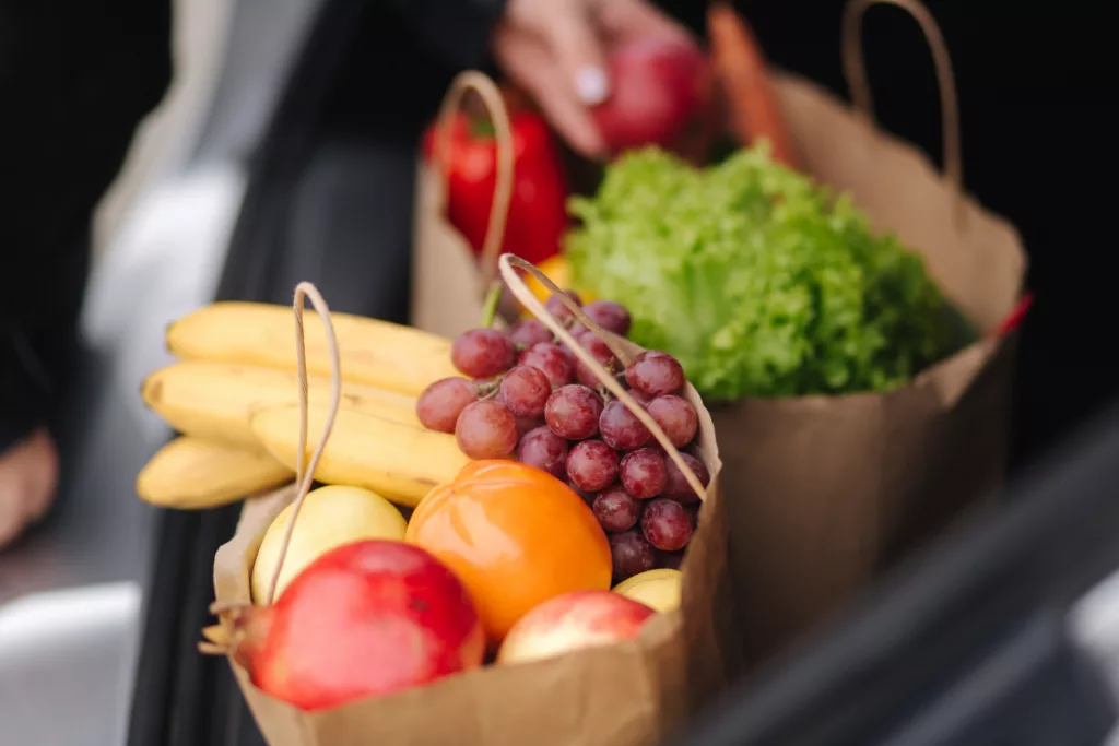 Sacs kraft contenant des courses fraîchement préparées avec des fruits et légumes de saison, illustrant la simplicité du drive Intermarché et des courses en ligne.