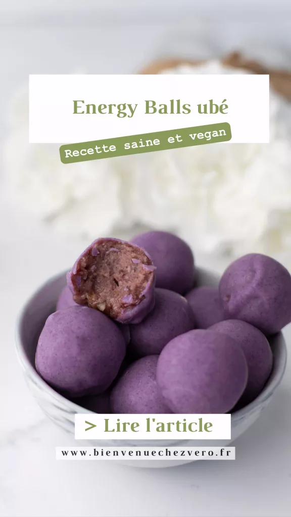 Energy balls ube - Petit bol rempli de boules violettes dont une est croquée sur le dessus. En fond et flouté, des fleurs blanches