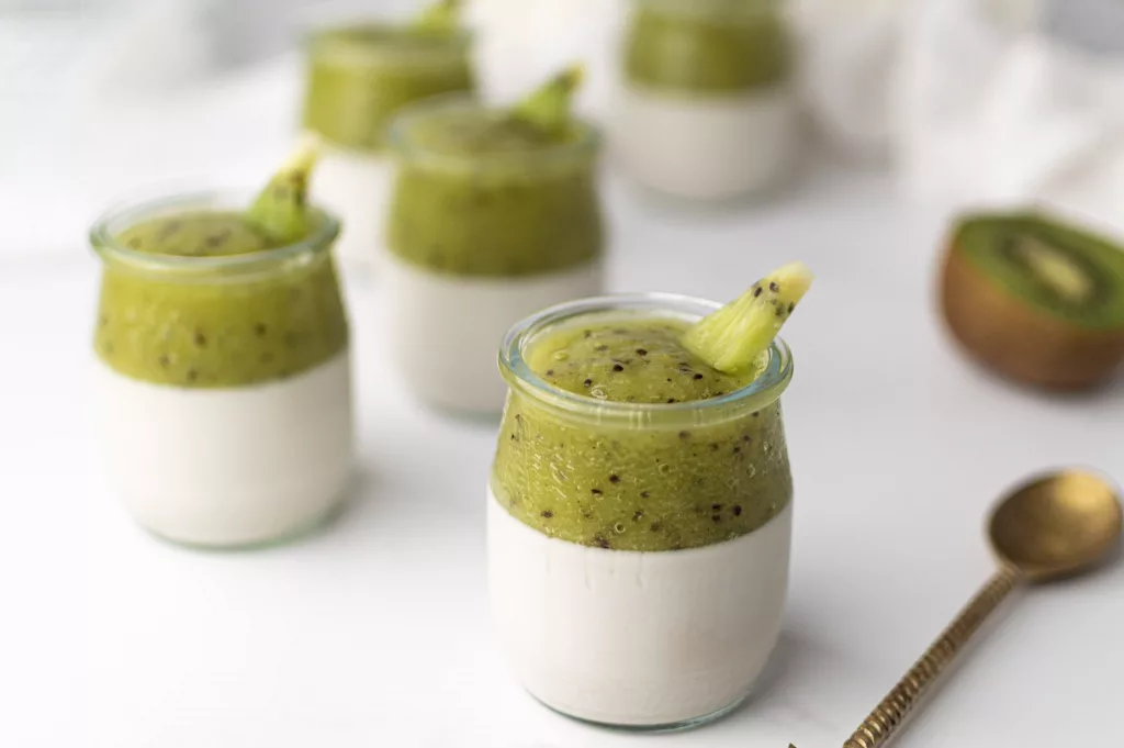 Verrines de panna cotta au lait de coco surmontées d'une purée de kiwi, servies dans des pots en verre sur fond blanc