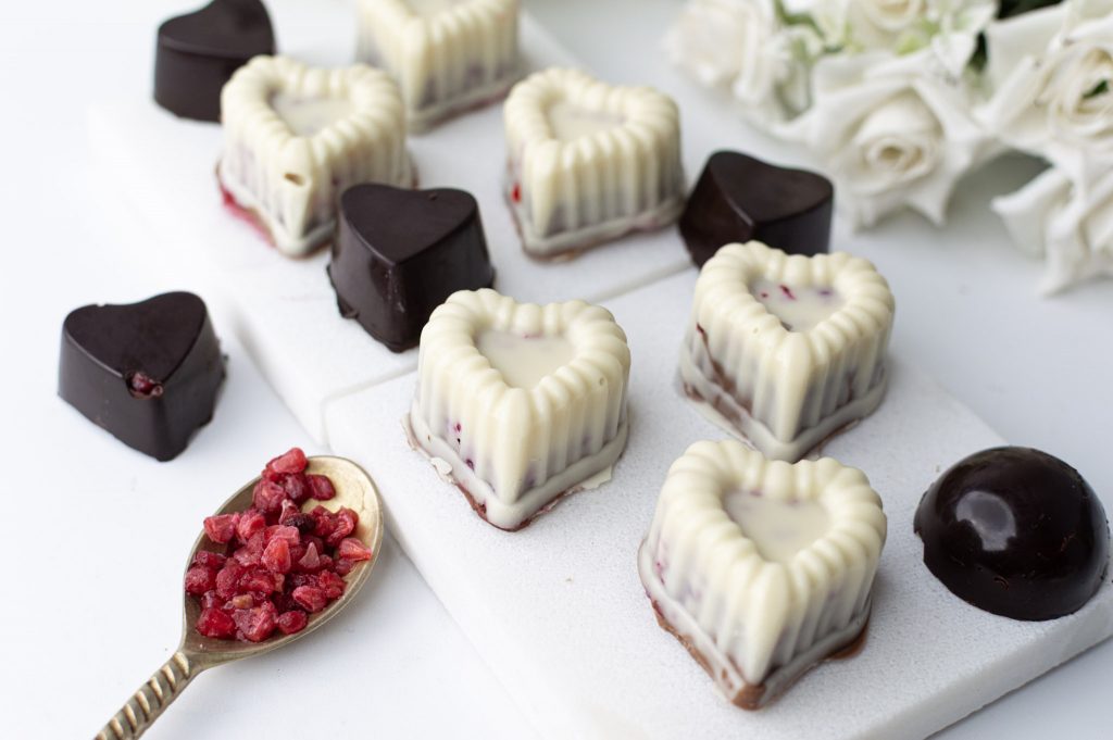Bouchées chocolat framboises façon Franui en forme de cœur, version chocolat blanc et chocolat noir 70 %, présentées sur ardoise en marbre avec framboises lyophilisées