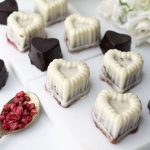 Bouchées chocolat framboises façon Franui en forme de cœur, version chocolat blanc et chocolat noir 70 %, présentées sur ardoise en marbre avec framboises lyophilisées