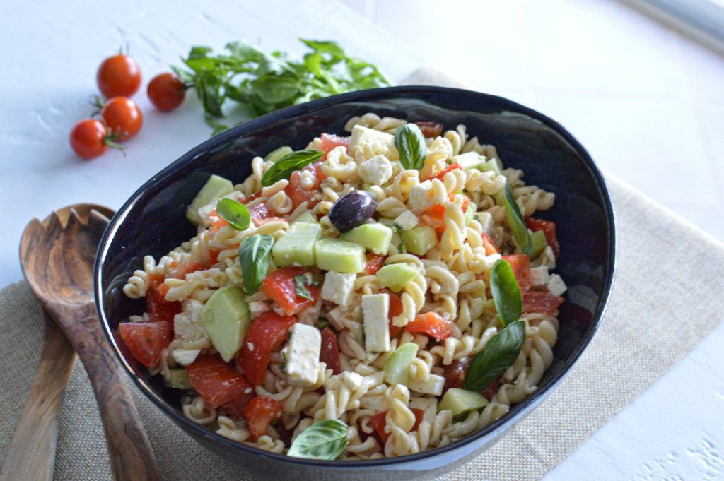 Salade de pâtes froide avec assaisonnement feta, tomates, concombre et basilic frais dans un saladier bleu foncé