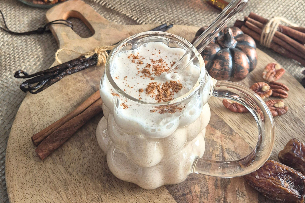 Lait de noix de pécan maison surmonté de mousse et de cannelle en poudre, servi dans une tasse en verre sur une planche en bois