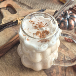 Lait de noix de pécan maison surmonté de mousse et de cannelle en poudre, servi dans une tasse en verre sur une planche en bois