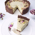Tarte pistache sans cuisson vegan entamée, une part sur assiette blanche, purée de pistache et boutons de rose séchés à côté